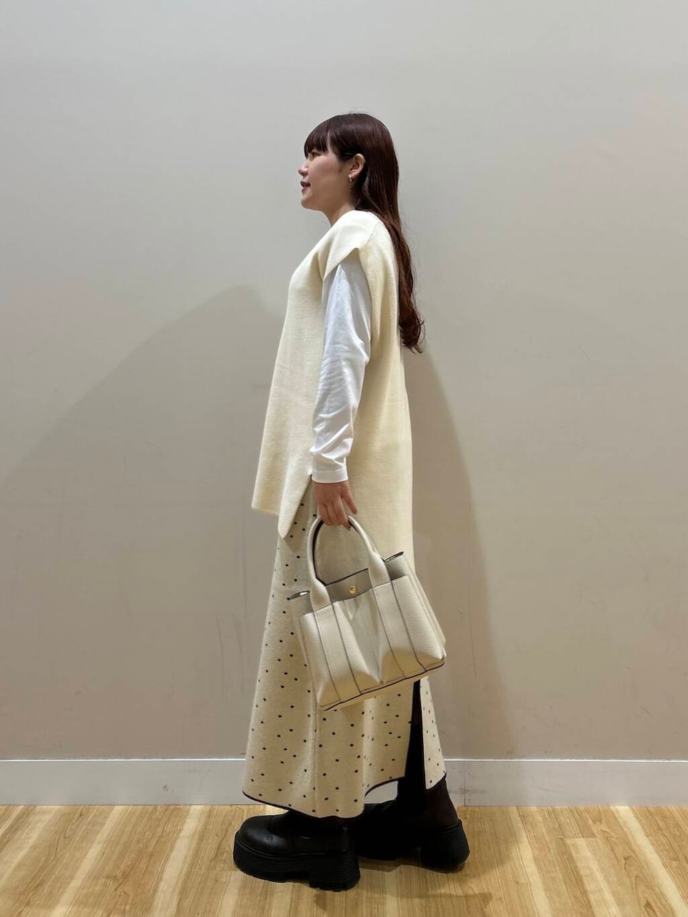 ブラウン系のハンドバッグ、ブラウン系のノーカラーコート、ホワイト系のスカートを着用したレディースの冬コーディネートの9枚目の写真