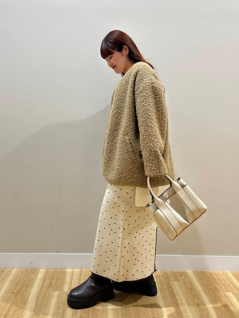 ブラウン系のハンドバッグ、ブラウン系のノーカラーコート、ホワイト系のスカートを着用したレディースの冬コーディネートの5枚目の写真