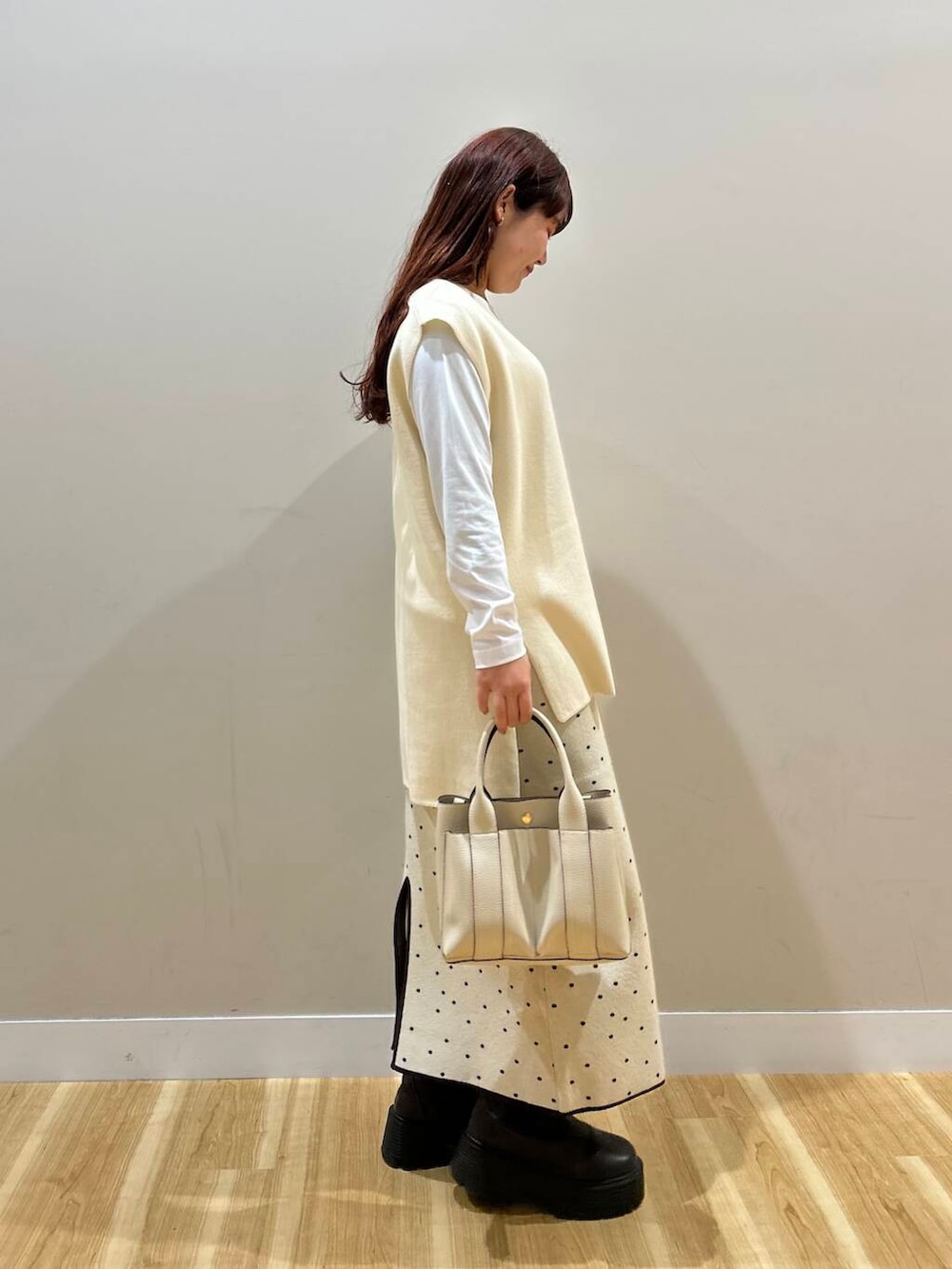 ブラウン系のハンドバッグ、ブラウン系のノーカラーコート、ホワイト系のスカートを着用したレディースの冬コーディネートの7枚目の写真