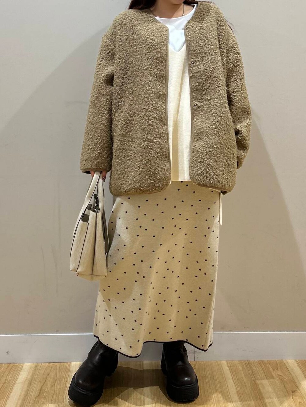 ブラウン系のハンドバッグ、ブラウン系のノーカラーコート、ホワイト系のスカートを着用したレディースの冬コーディネートの6枚目の写真