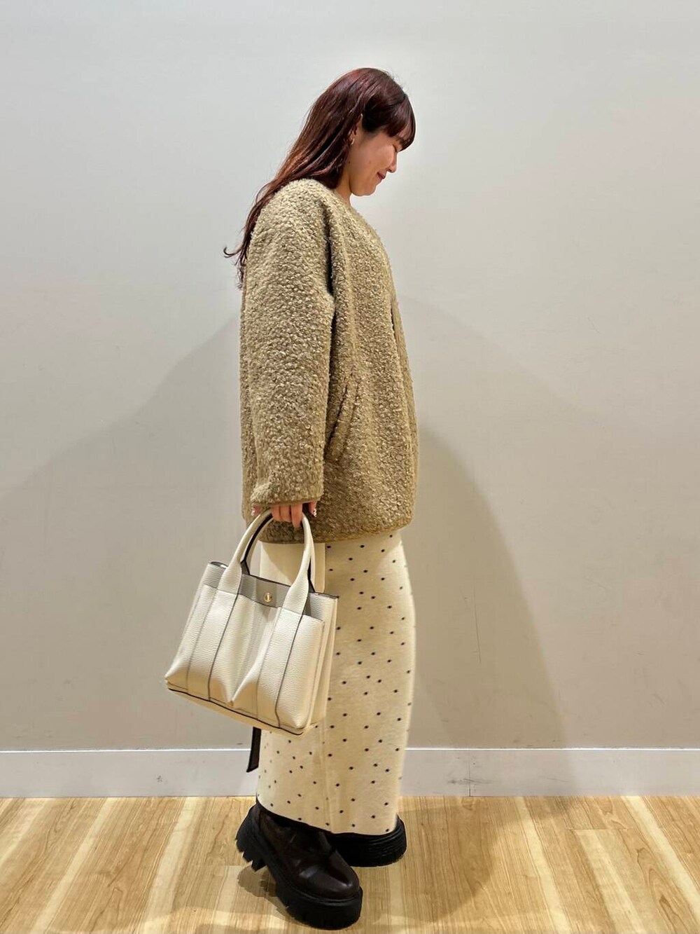 ブラウン系のハンドバッグ、ブラウン系のノーカラーコート、ホワイト系のスカートを着用したレディースの冬コーディネートの3枚目の写真