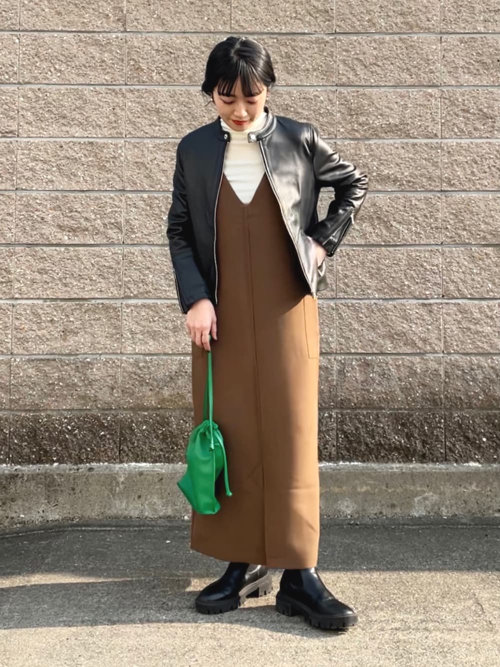 ブラック系のライダースジャケット、ブラウン系のジャンパースカート、グリーン系のショルダーバッグを着用したレディースの冬コーディネートの2枚目の写真