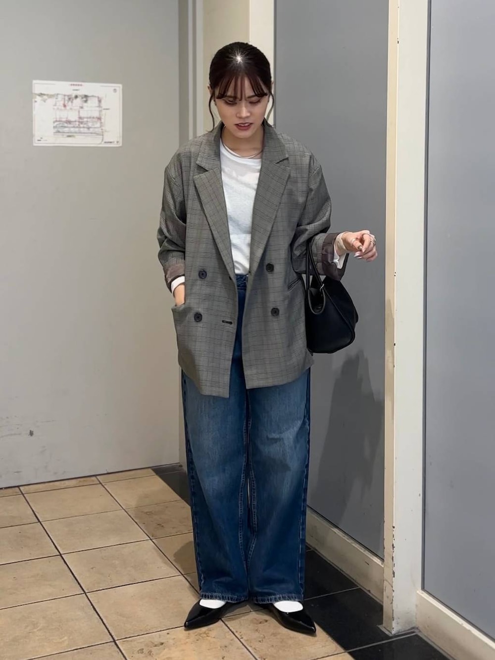 グレー系のテーラードジャケット、ブラック系のショルダーバッグ、ブルー系のデニムパンツを着用したレディースの秋コーディネートの2枚目の写真