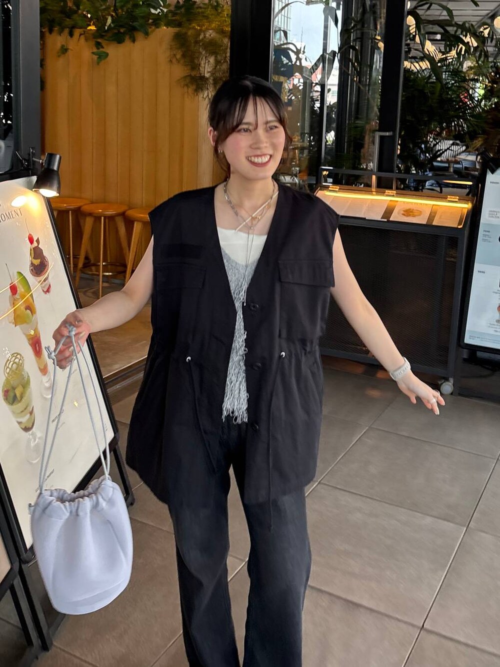 グレー系のショルダーバッグ、ブラック系のサンダル、ホワイト系のベストを着用したレディースの夏コーディネートの2枚目の写真