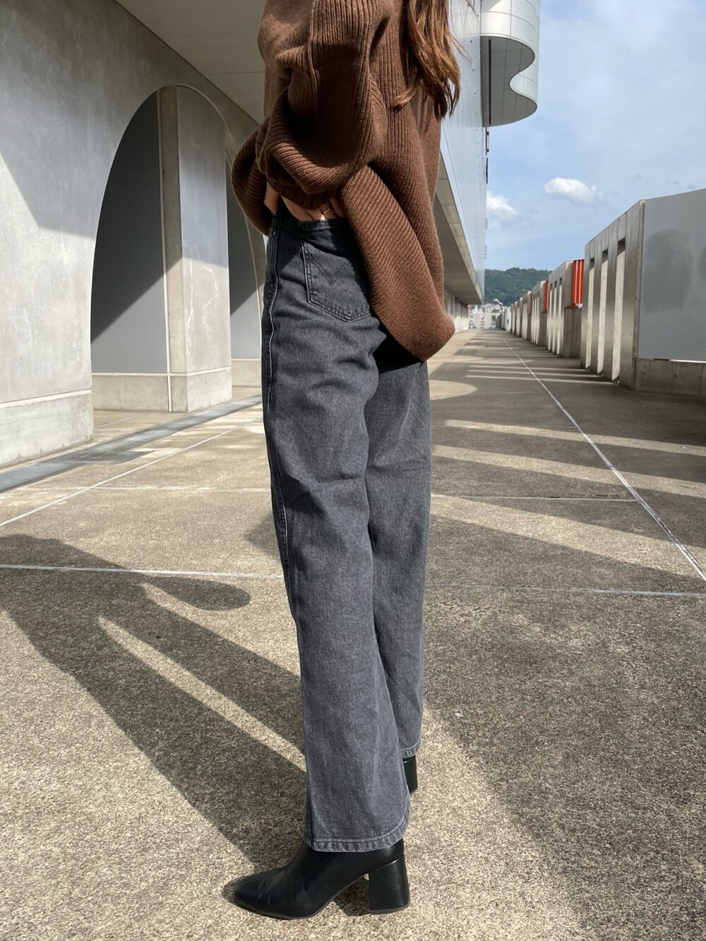 ブラウン系のニット/セーター、ブラック系のデニムパンツ、ホワイト系のハンドバッグを着用したレディースの秋コーディネートの3枚目の写真