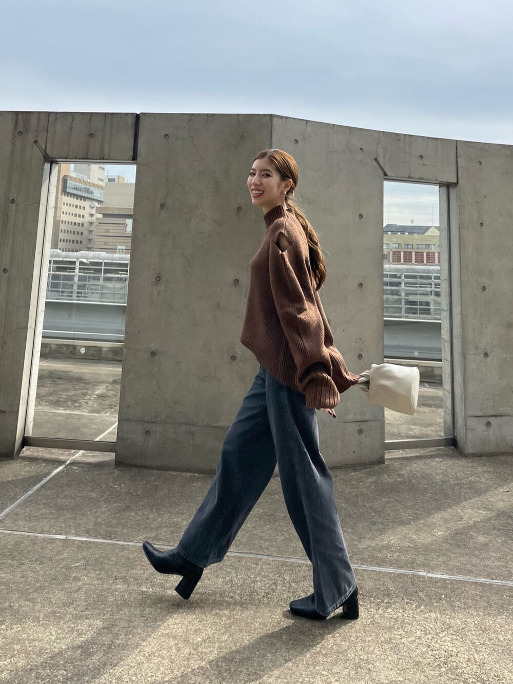 ブラウン系のニット/セーター、ブラック系のデニムパンツ、ホワイト系のハンドバッグを着用したレディースの秋コーディネートの5枚目の写真