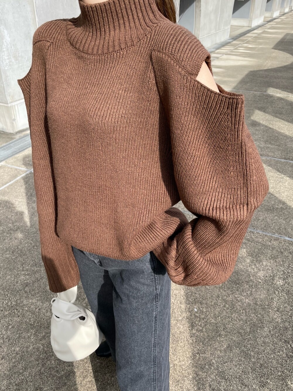 ブラウン系のニット/セーター、ブラック系のデニムパンツ、ホワイト系のハンドバッグを着用したレディースの秋コーディネートの6枚目の写真