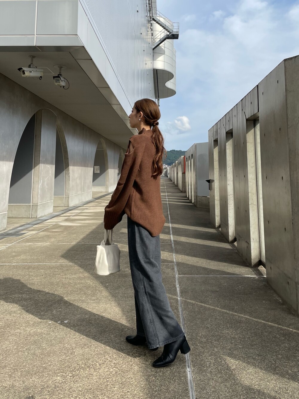 ブラウン系のニット/セーター、ブラック系のデニムパンツ、ホワイト系のハンドバッグを着用したレディースの秋コーディネートの2枚目の写真