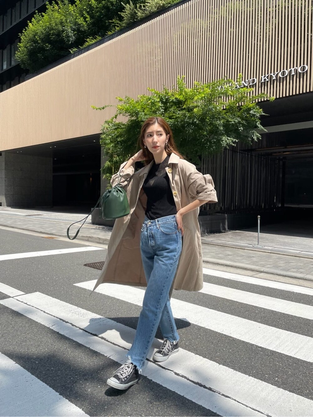 ベージュ系のステンカラーコート、ブラック系のニット/セーター、ブルー系のデニムパンツを着用したレディースの夏コーディネートの3枚目の写真