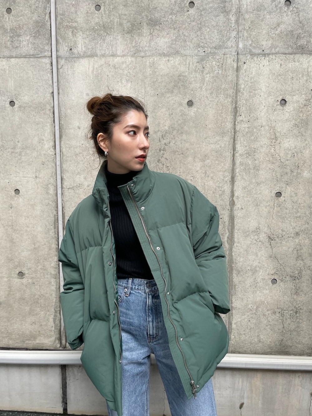 ブルー系のデニムパンツ、グリーン系のダウンジャケット/コート、ブラック系のニット/セーターを着用したレディースの秋コーディネートの2枚目の写真