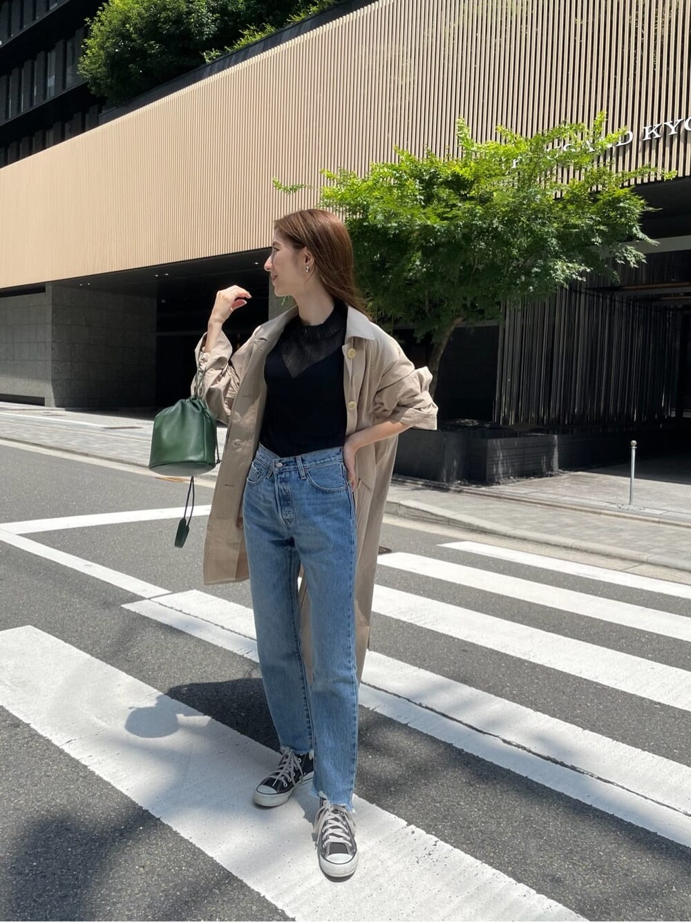 ベージュ系のステンカラーコート、ブラック系のニット/セーター、ブルー系のデニムパンツを着用したレディースの夏コーディネートの4枚目の写真