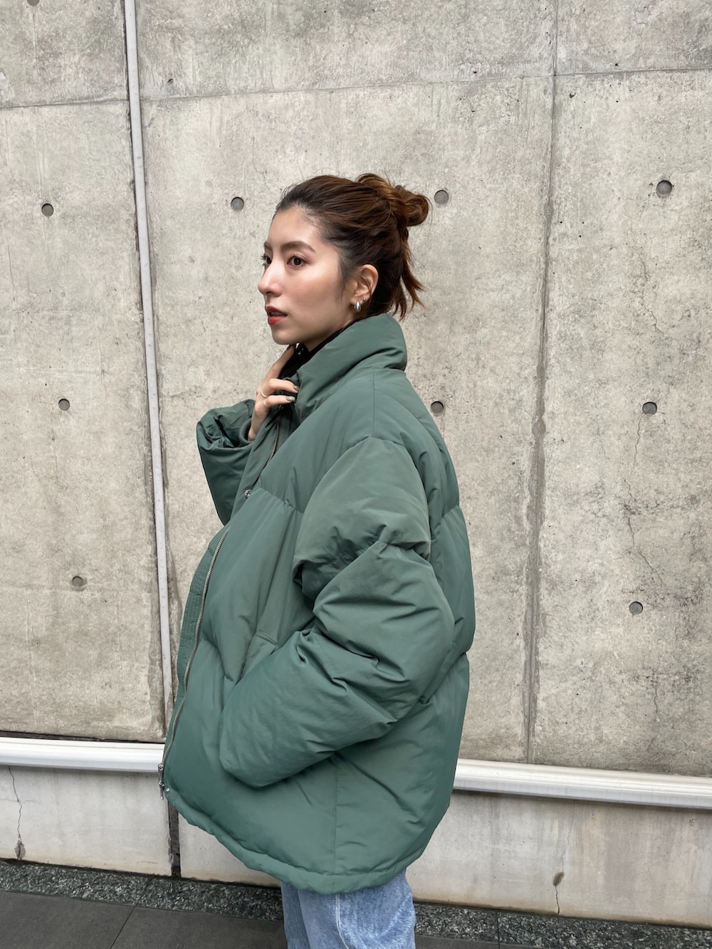 ブルー系のデニムパンツ、グリーン系のダウンジャケット/コート、ブラック系のニット/セーターを着用したレディースの秋コーディネートの3枚目の写真