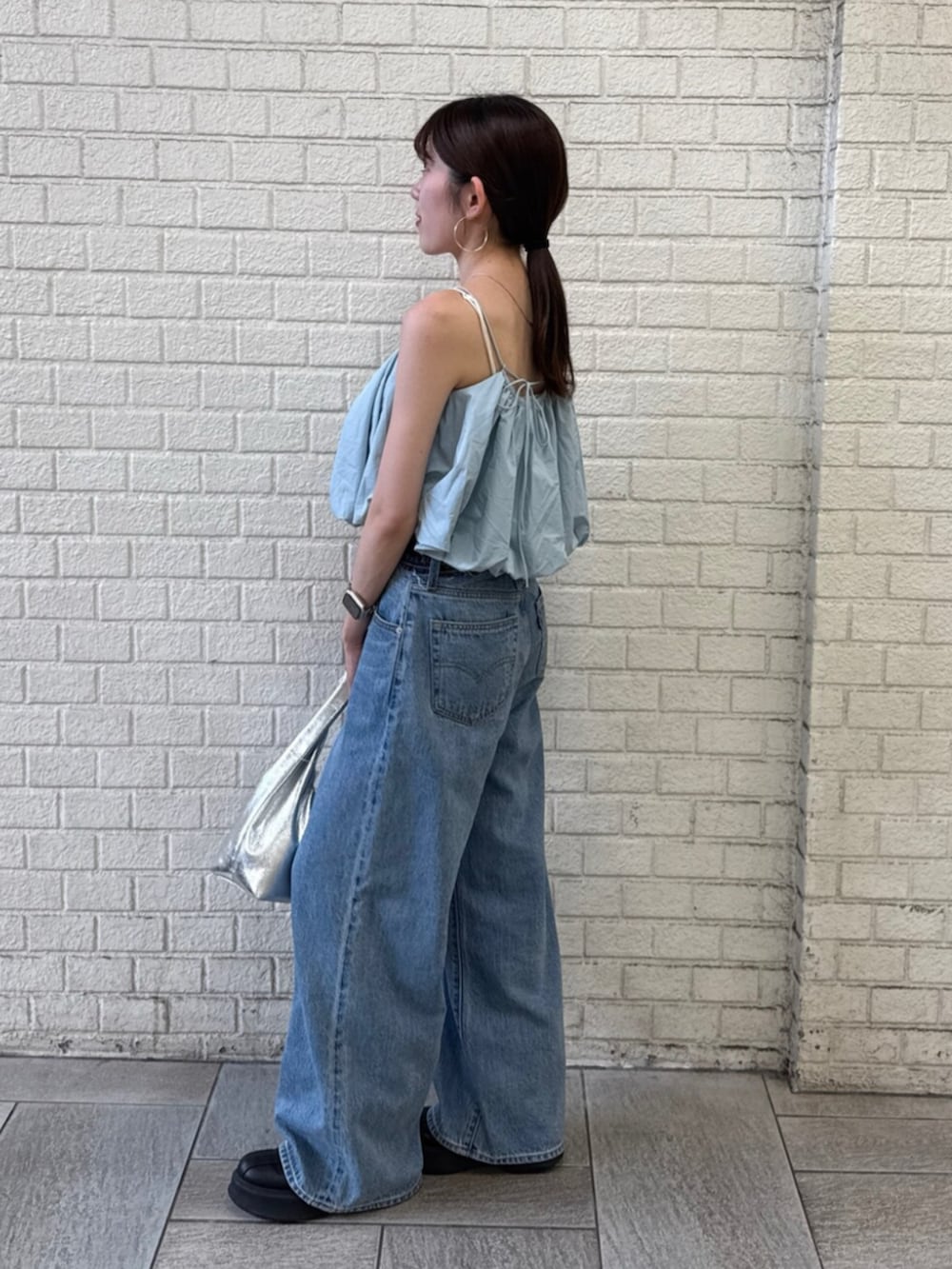 シルバー系のハンドバッグ、ブルー系のデニムパンツ、ブルー系のキャミソールを着用したレディースの夏コーディネートの6枚目の写真