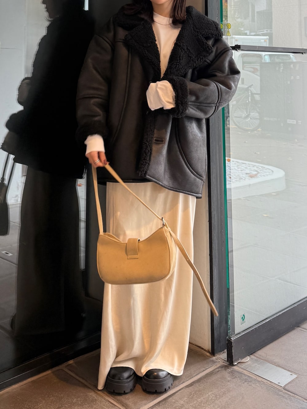 ブラック系のブルゾン、ベージュ系のハンドバッグ、ホワイト系のスカートを着用したレディースの冬コーディネートの2枚目の写真