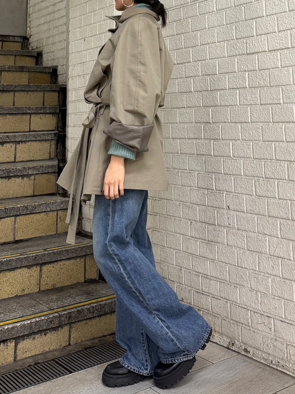 グリーン系のトレンチコート、グリーン系のニット/セーター、ブルー系のデニムパンツを着用したレディースの冬コーディネートの4枚目の写真