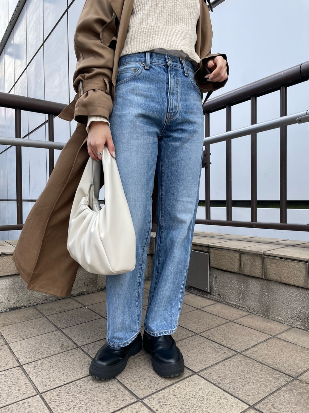 ホワイト系のハンドバッグ、ホワイト系のTシャツ/カットソー、ブルー系のデニムパンツを着用したレディースの冬コーディネートの6枚目の写真