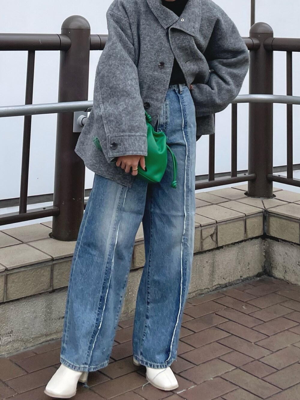 ブルー系のデニムパンツ、ホワイト系のブーツ、グリーン系のクラッチバッグを着用したレディースの秋コーディネートの3枚目の写真