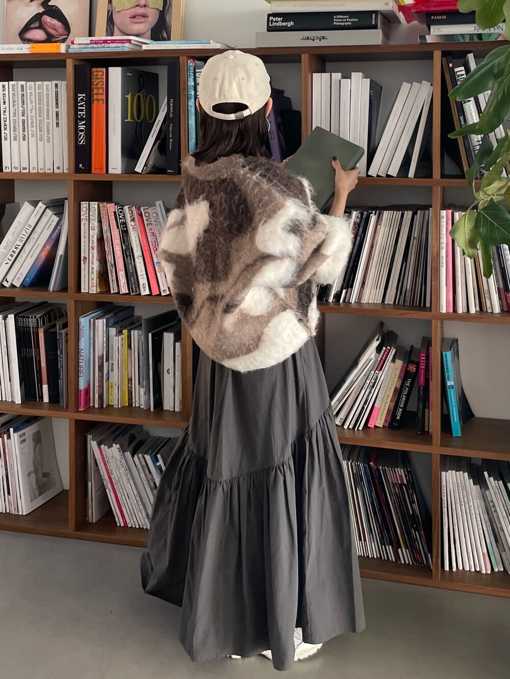 グレー系のスカート、ベージュ系のニット/セーター、ホワイト系のキャップを着用したレディースの秋コーディネートの2枚目の写真