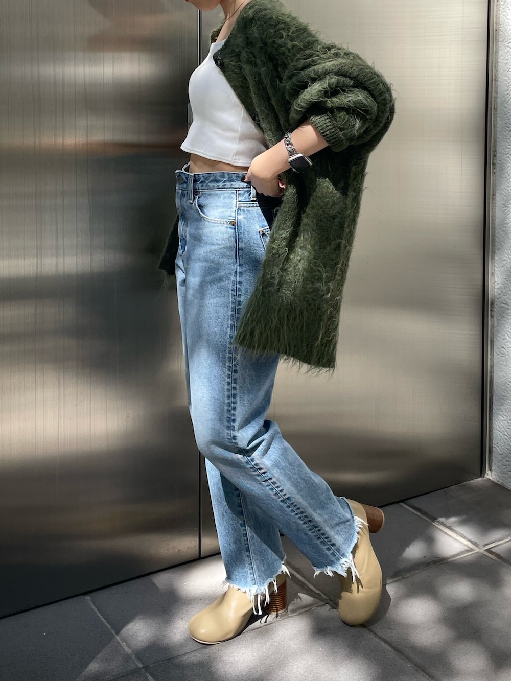 グリーン系のカーディガン/ボレロ、ベージュ系のブーツ、ブルー系のデニムパンツを着用したレディースの秋コーディネートの4枚目の写真