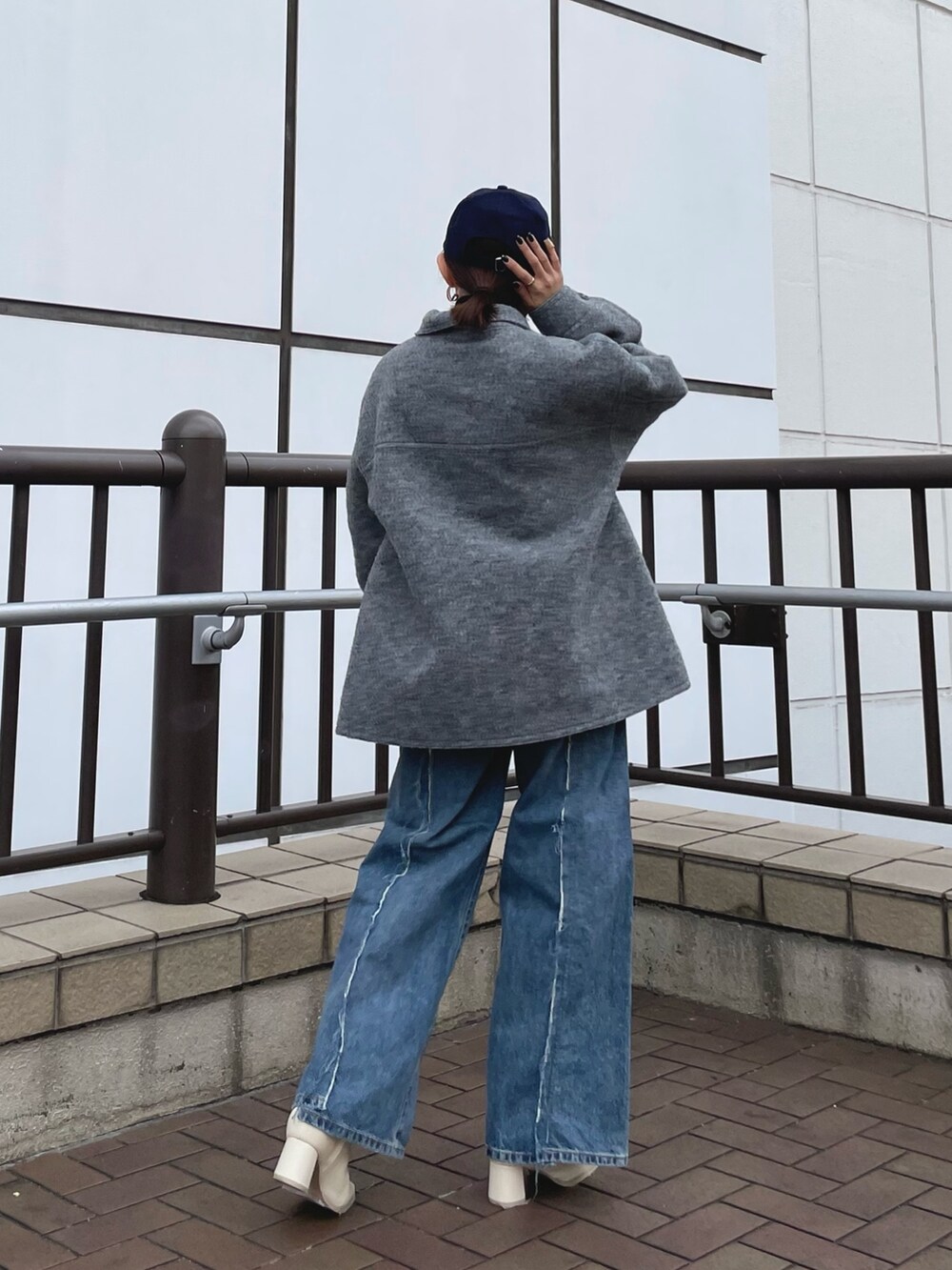 ブルー系のデニムパンツ、ホワイト系のブーツ、グリーン系のクラッチバッグを着用したレディースの秋コーディネートの2枚目の写真