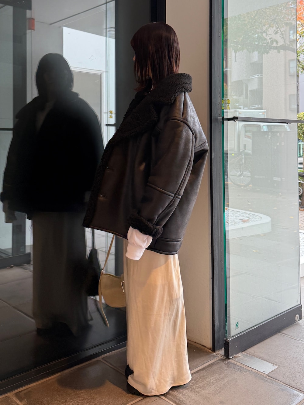 ブラック系のブルゾン、ベージュ系のハンドバッグ、ホワイト系のスカートを着用したレディースの冬コーディネートの3枚目の写真