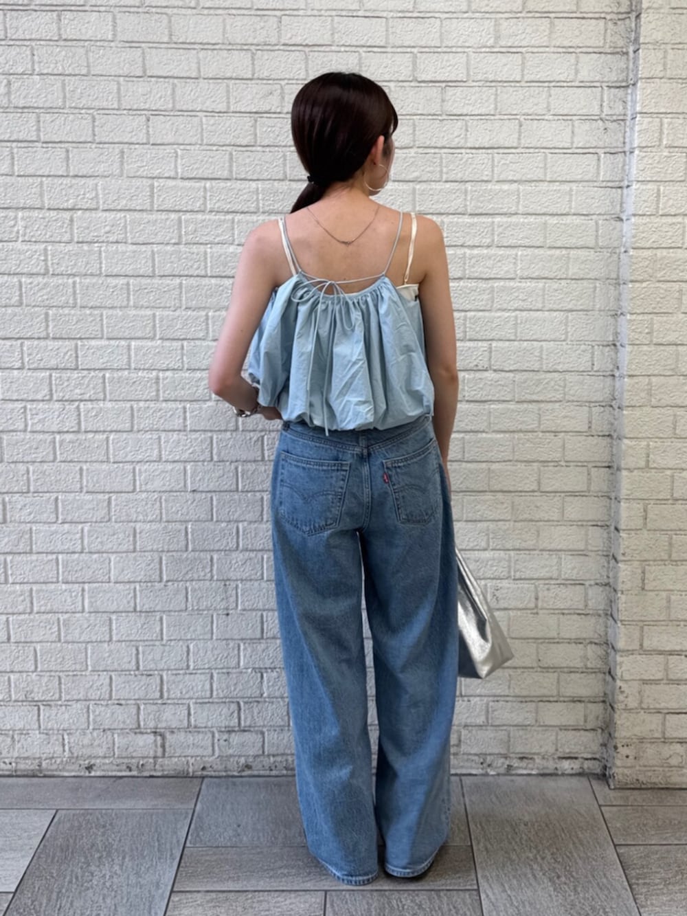 シルバー系のハンドバッグ、ブルー系のデニムパンツ、ブルー系のキャミソールを着用したレディースの夏コーディネートの4枚目の写真