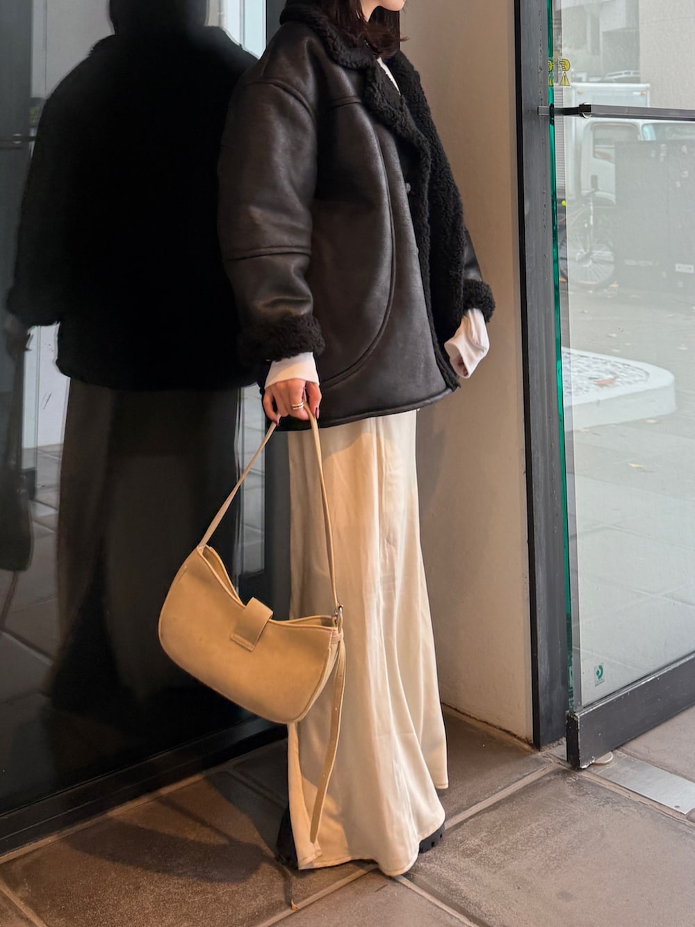 ブラック系のブルゾン、ベージュ系のハンドバッグ、ホワイト系のスカートを着用したレディースの冬コーディネートの5枚目の写真