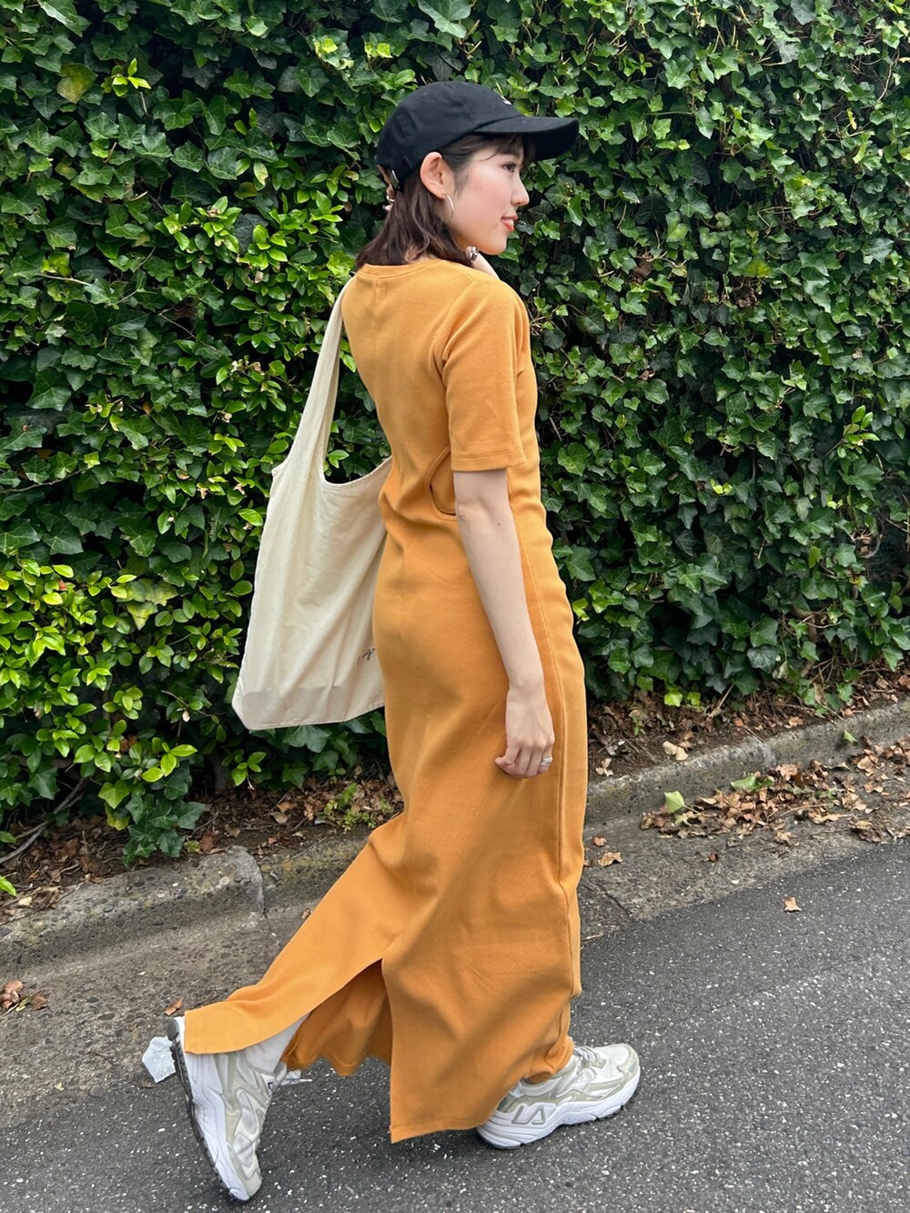 オレンジ系のワンピース、ホワイト系のエコバッグ/サブバッグ、ブラック系のキャップを着用したレディースの夏コーディネートの2枚目の写真