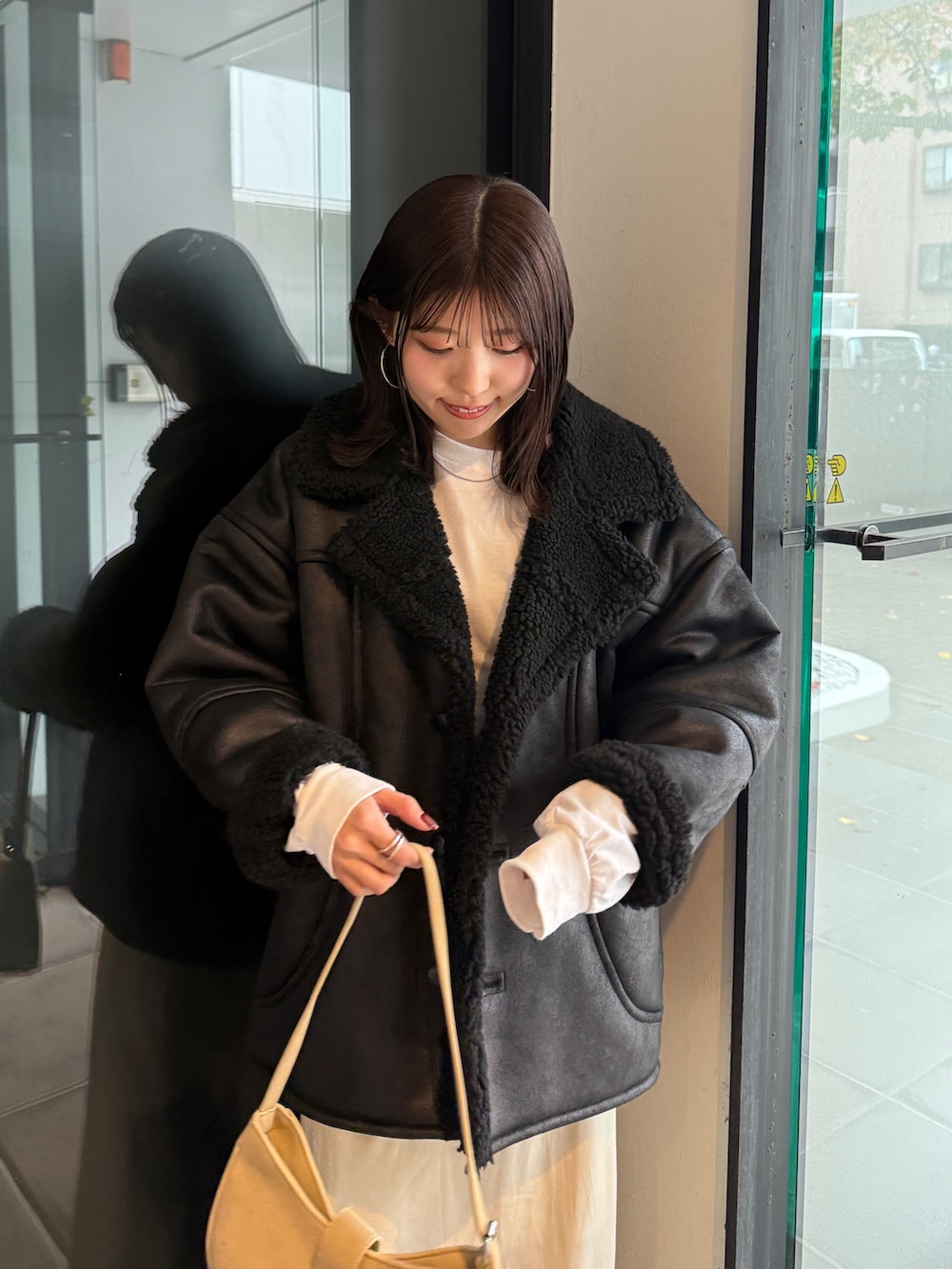 ブラック系のブルゾン、ベージュ系のハンドバッグ、ホワイト系のスカートを着用したレディースの冬コーディネートの6枚目の写真