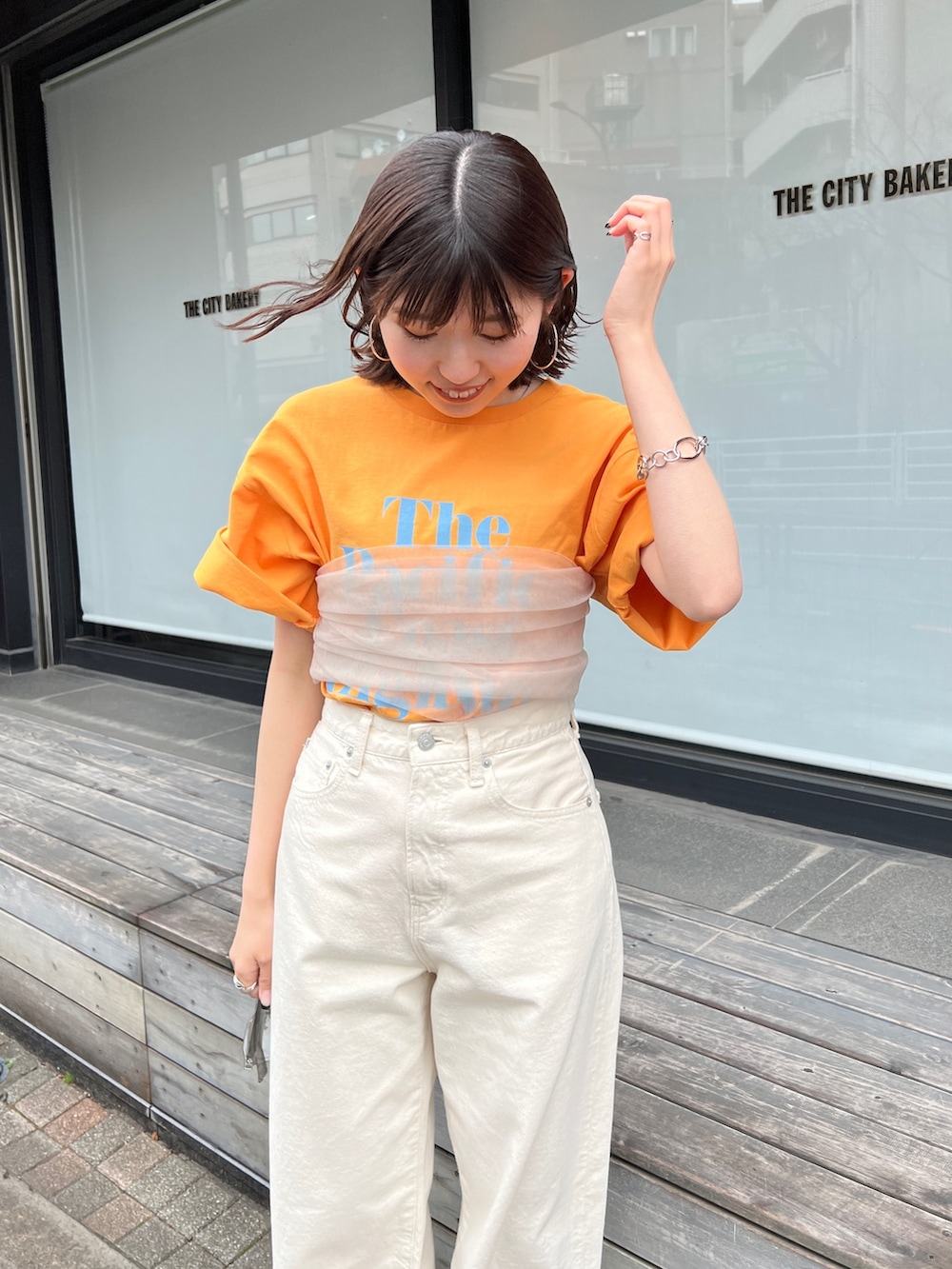 ホワイト系のデニムパンツ、ブラック系のサンダル、オレンジ系のTシャツ/カットソーを着用したレディースの春コーディネートの3枚目の写真