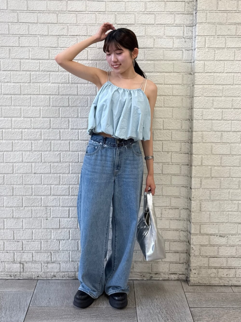 シルバー系のハンドバッグ、ブルー系のデニムパンツ、ブルー系のキャミソールを着用したレディースの夏コーディネートの2枚目の写真