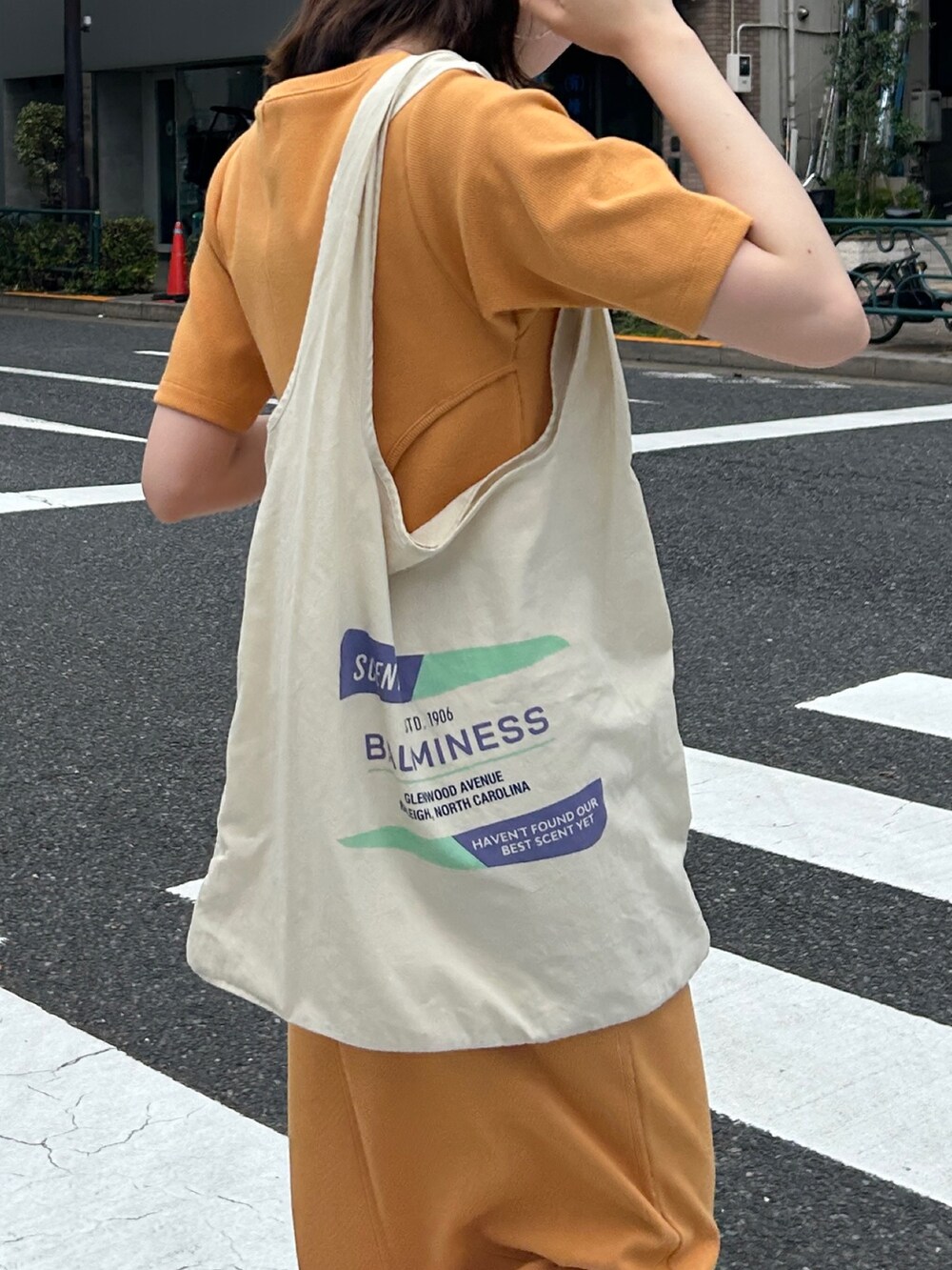 オレンジ系のワンピース、ホワイト系のエコバッグ/サブバッグ、ブラック系のキャップを着用したレディースの夏コーディネートの9枚目の写真
