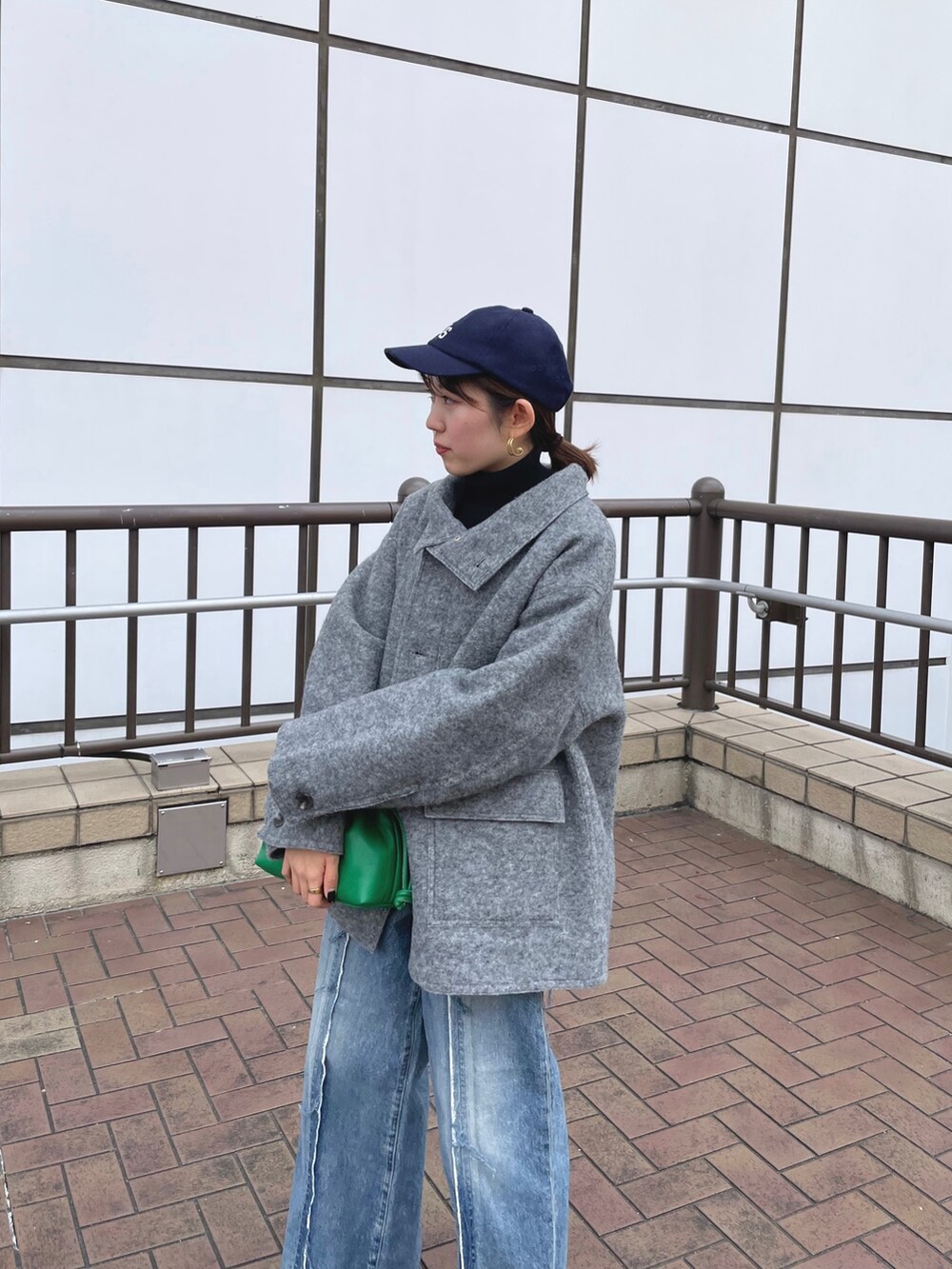 ブルー系のデニムパンツ、ホワイト系のブーツ、グリーン系のクラッチバッグを着用したレディースの秋コーディネートの5枚目の写真