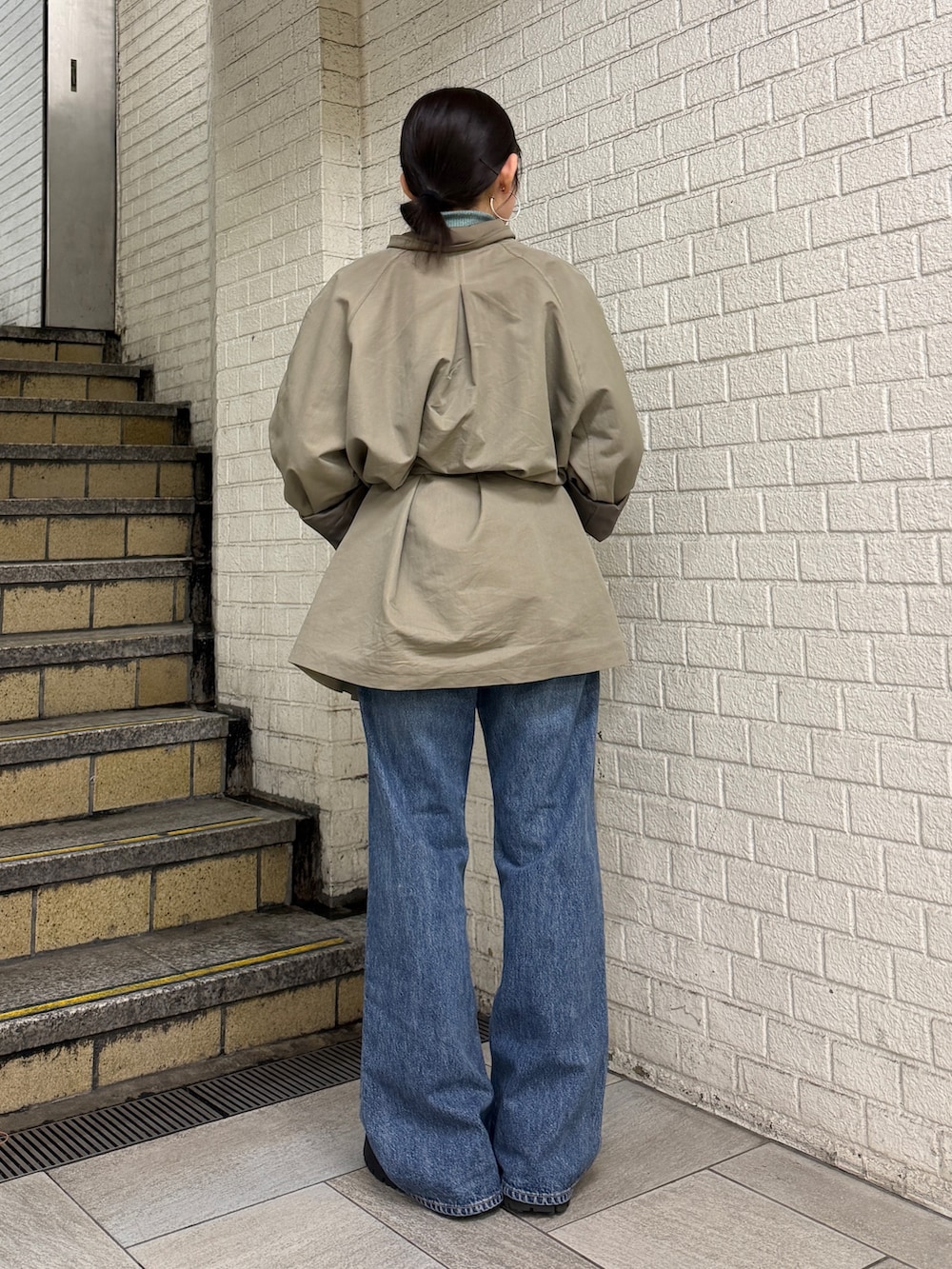 グリーン系のトレンチコート、グリーン系のニット/セーター、ブルー系のデニムパンツを着用したレディースの冬コーディネートの3枚目の写真