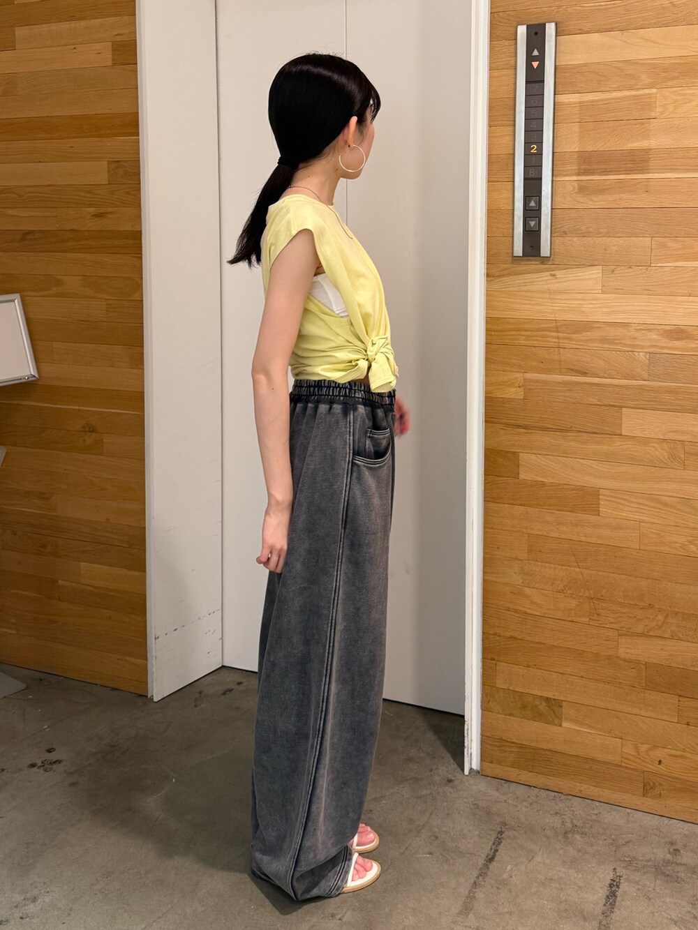 グレー系のスウェットパンツ、イエロー系のタンクトップ、ホワイト系のサンダルを着用したレディースの夏コーディネートの2枚目の写真