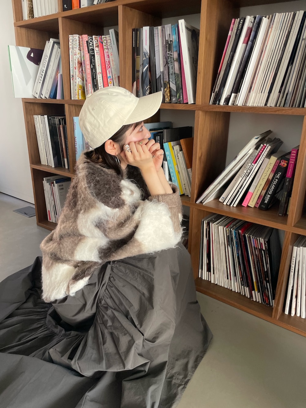 グレー系のスカート、ベージュ系のニット/セーター、ホワイト系のキャップを着用したレディースの秋コーディネートの3枚目の写真