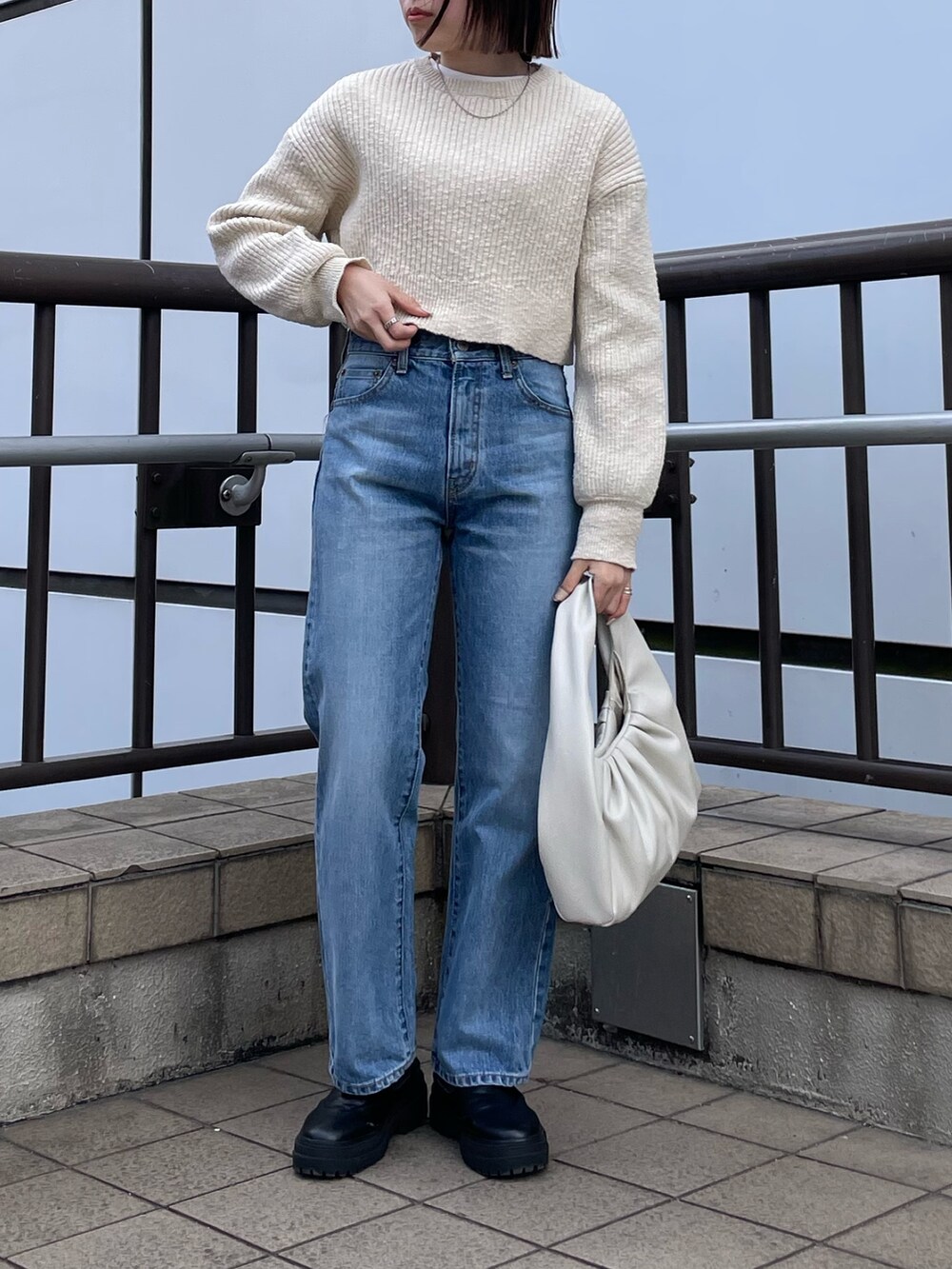 ホワイト系のハンドバッグ、ホワイト系のTシャツ/カットソー、ブルー系のデニムパンツを着用したレディースの冬コーディネートの4枚目の写真