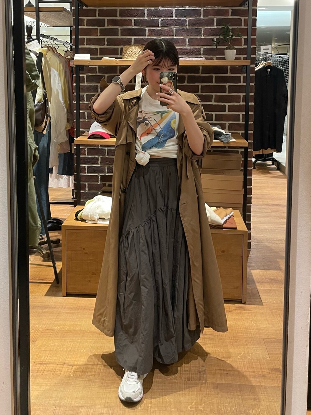 イエロー系のトレンチコート、グレー系のスカート、ホワイト系のTシャツ/カットソーを着用したレディースの春コーディネートの2枚目の写真