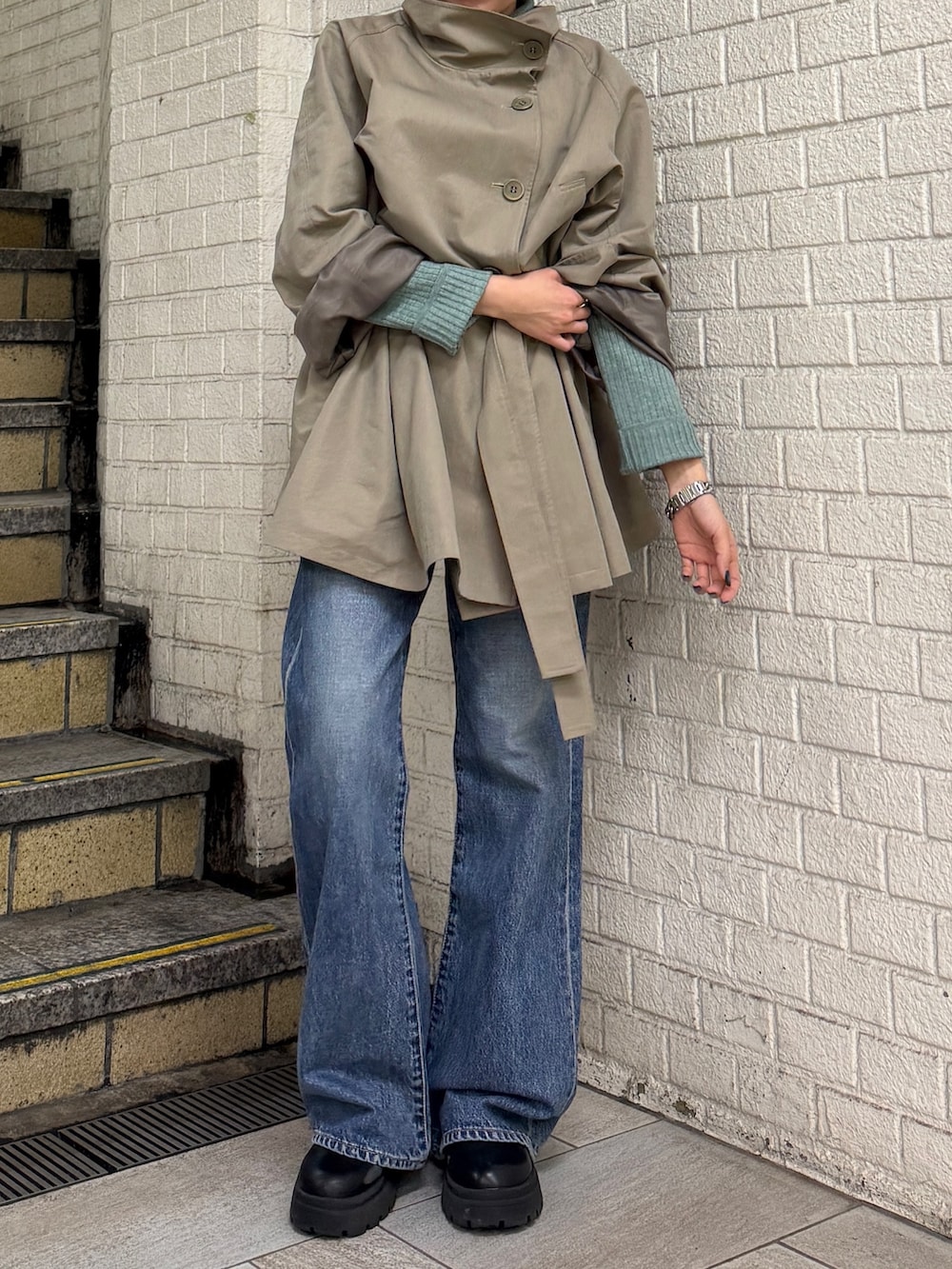 グリーン系のトレンチコート、グリーン系のニット/セーター、ブルー系のデニムパンツを着用したレディースの冬コーディネートの6枚目の写真