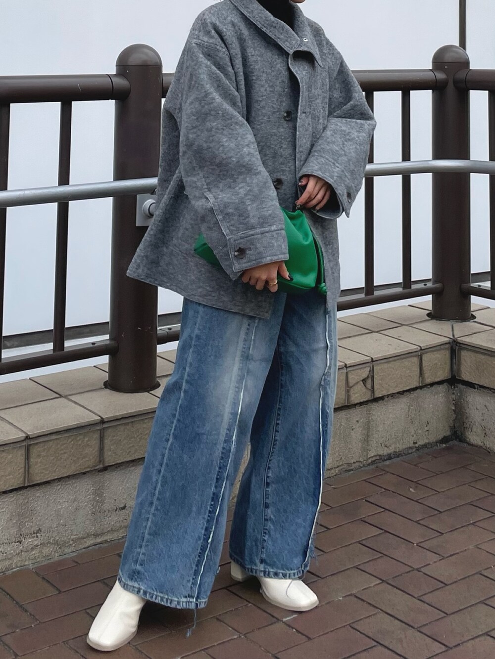 ブルー系のデニムパンツ、ホワイト系のブーツ、グリーン系のクラッチバッグを着用したレディースの秋コーディネートの4枚目の写真