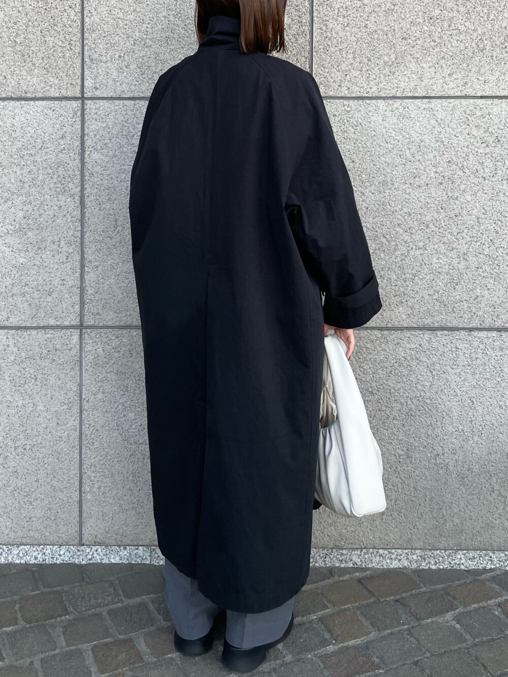 ホワイト系のハンドバッグ、ブラック系のステンカラーコート、グレー系のその他パンツを着用したレディースの春コーディネートの7枚目の写真