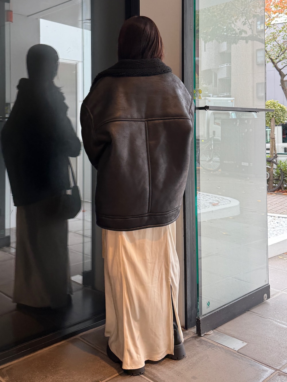 ブラック系のブルゾン、ベージュ系のハンドバッグ、ホワイト系のスカートを着用したレディースの冬コーディネートの4枚目の写真