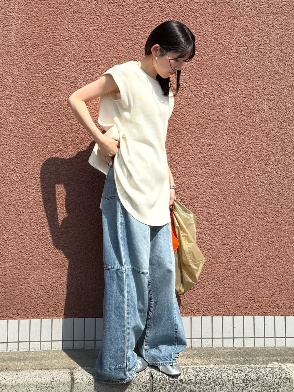 ホワイト系のタンクトップ、ブルー系のデニムパンツ、ベージュ系のショルダーバッグを着用したレディースの夏コーディネートの3枚目の写真