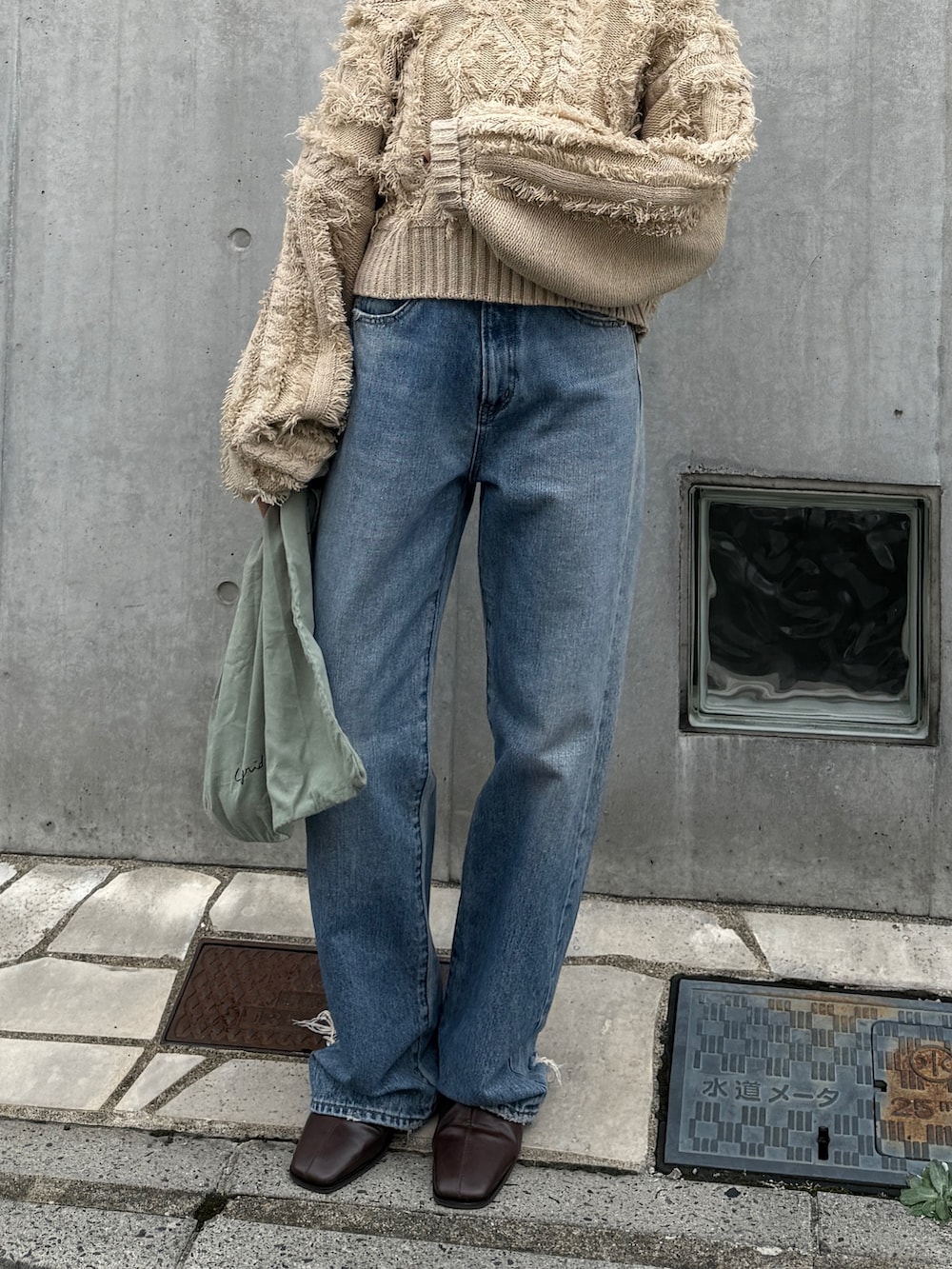 ブルー系のデニムパンツ、グリーン系のトートバッグ、ブラウン系のブーツを着用したレディースの秋コーディネートの4枚目の写真