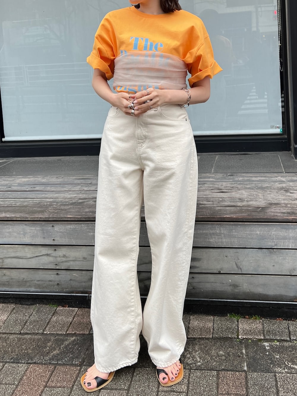 ホワイト系のデニムパンツ、ブラック系のサンダル、オレンジ系のTシャツ/カットソーを着用したレディースの春コーディネートの2枚目の写真
