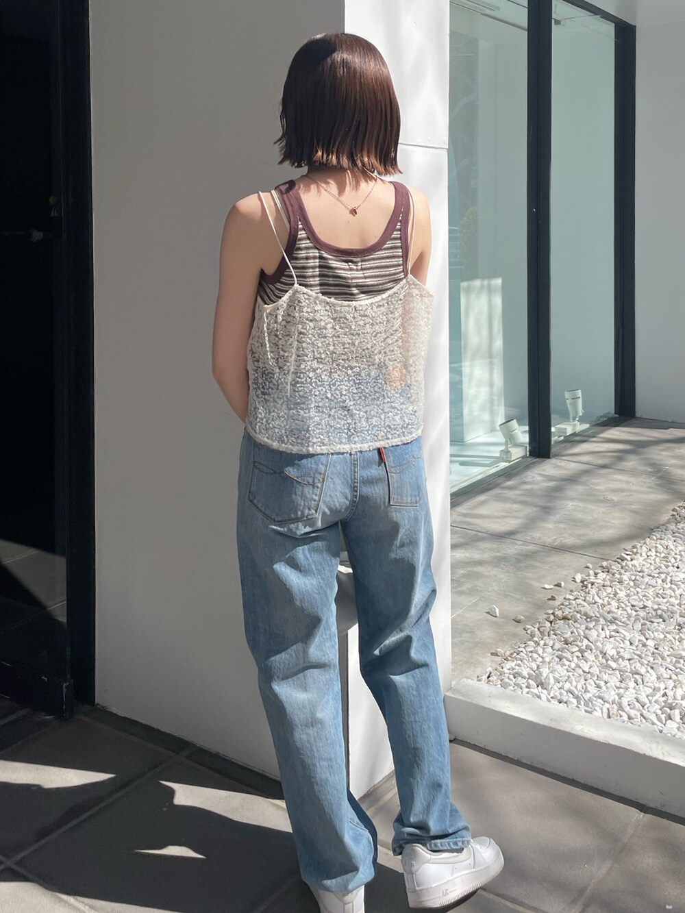 ホワイト系のハンドバッグ、ブルー系のデニムパンツ、ホワイト系のキャミソールを着用したレディースの春コーディネートの2枚目の写真