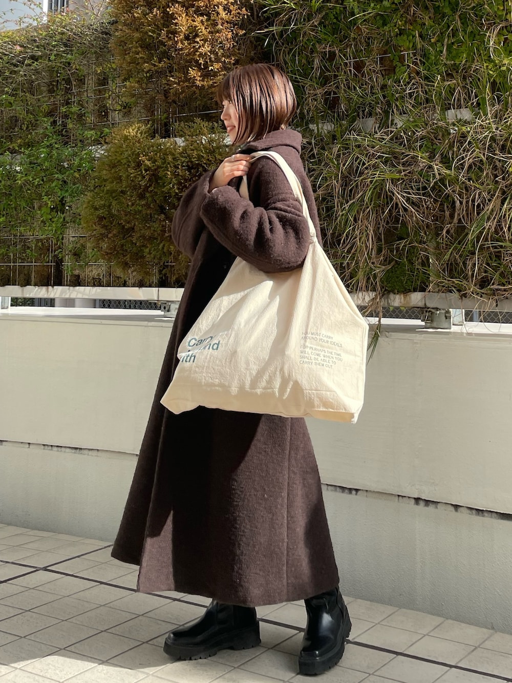 グリーン系のニット/セーター、ブラウン系のチェスターコート、ホワイト系のハンドバッグを着用したレディースの冬コーディネートの6枚目の写真