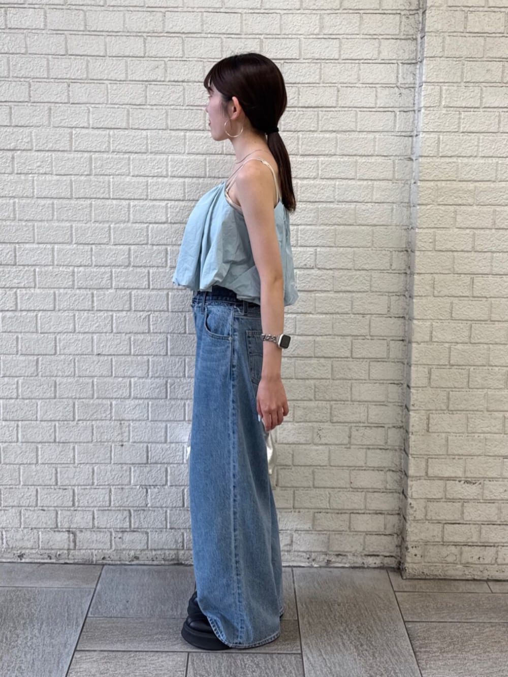 シルバー系のハンドバッグ、ブルー系のデニムパンツ、ブルー系のキャミソールを着用したレディースの夏コーディネートの3枚目の写真