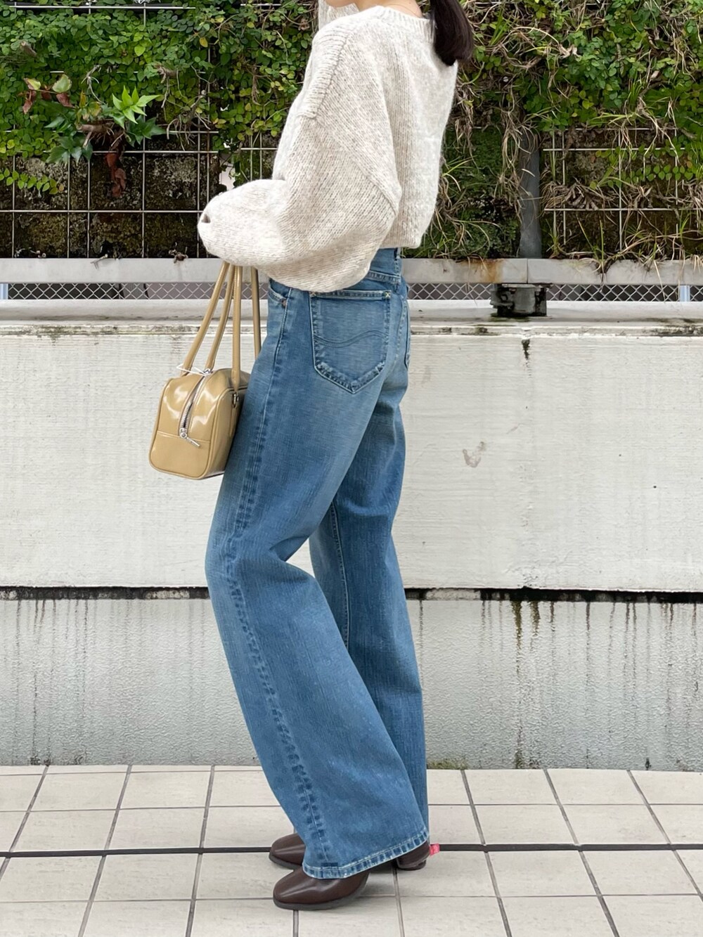 ブルー系のデニムパンツ、ブラウン系のブーツ、ベージュ系のハンドバッグを着用したレディースの秋コーディネートの7枚目の写真