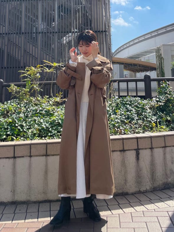 ブラウン系のトレンチコート、ブラック系のブーツ、ホワイト系のワンピースを着用したレディースの秋コーディネートの2枚目の写真